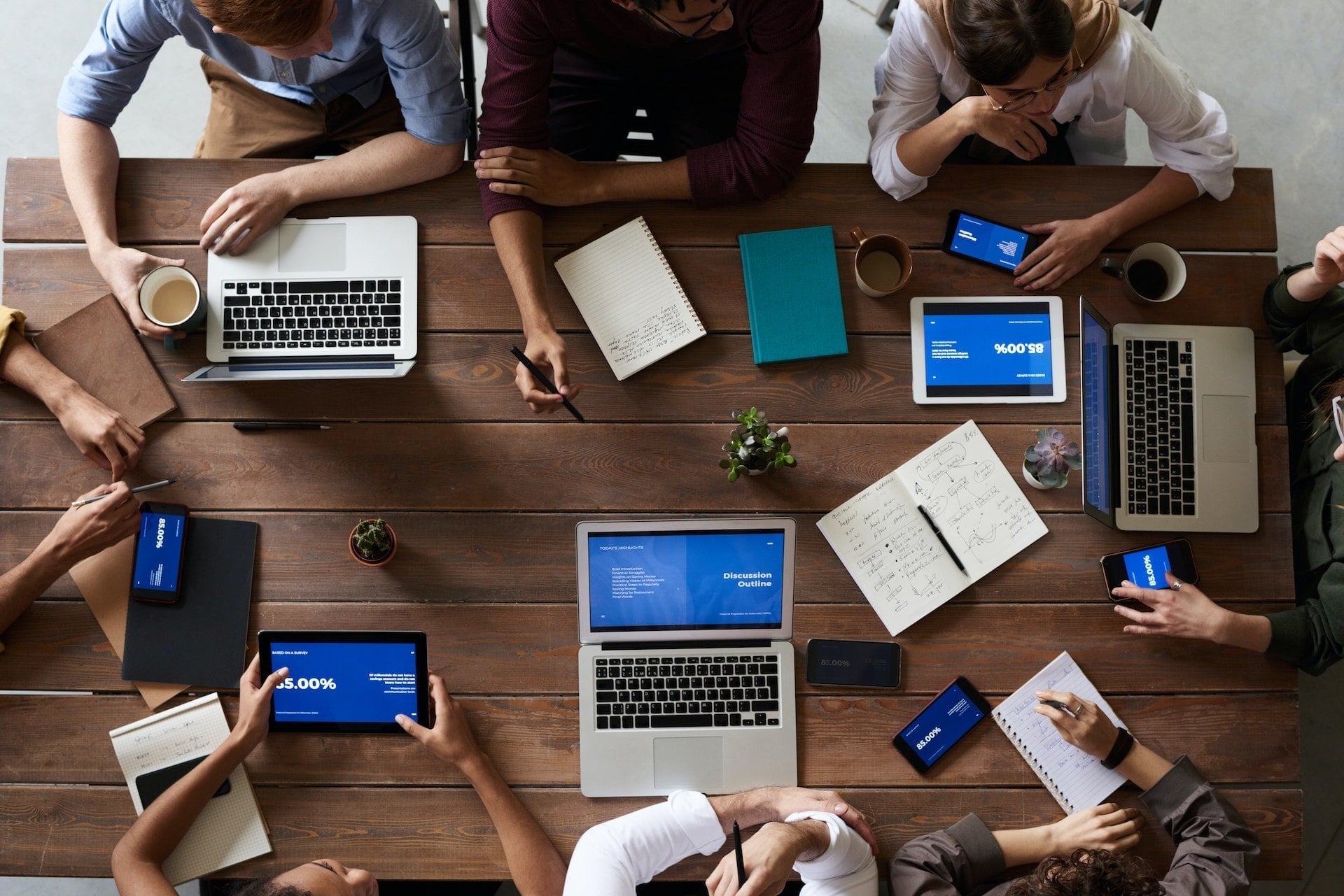 Blick von oben auf einen mit Laptops und Notizblöcken übersäten Schreibtisch, auf dem eine Strategiesitzung stattfindet