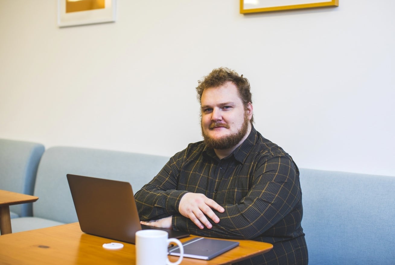 Bearded man in flannel shirt sits with laptop